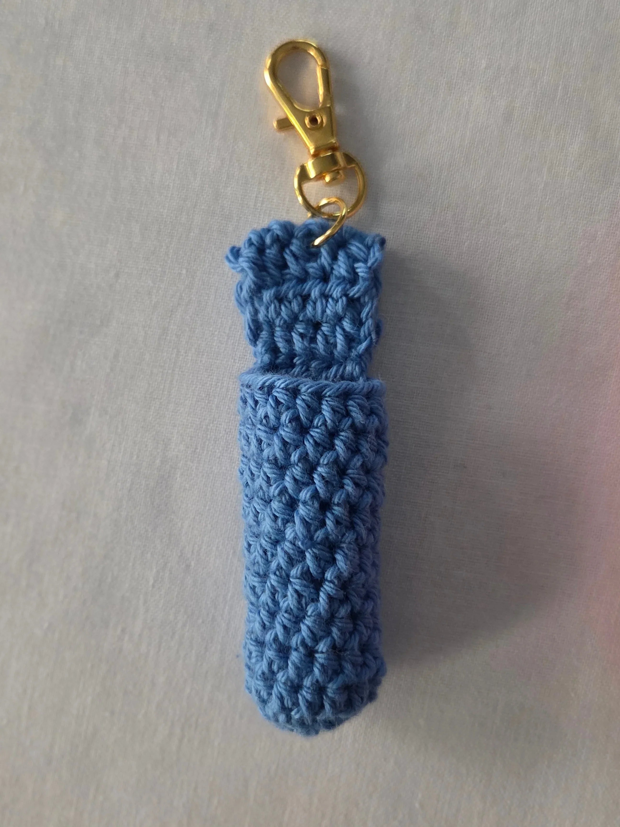 Blue crocheted keychain with a gold clasp on a light gray background