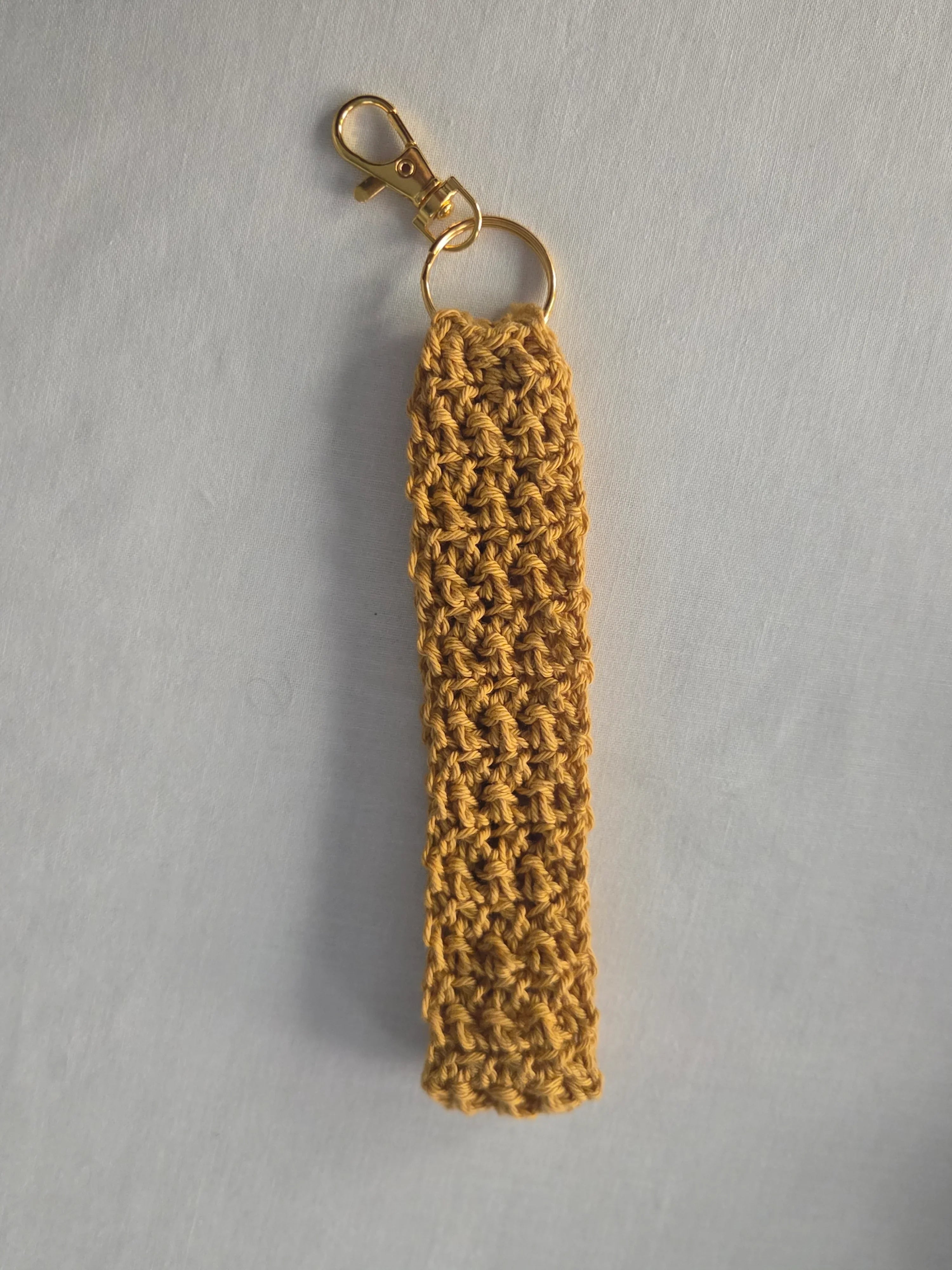 Handmade mustard yellow crochet keychain with gold clasp on white background