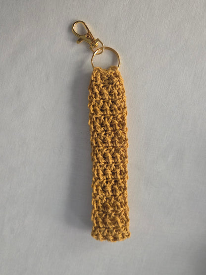 Handmade mustard yellow crochet keychain with gold clasp on white background