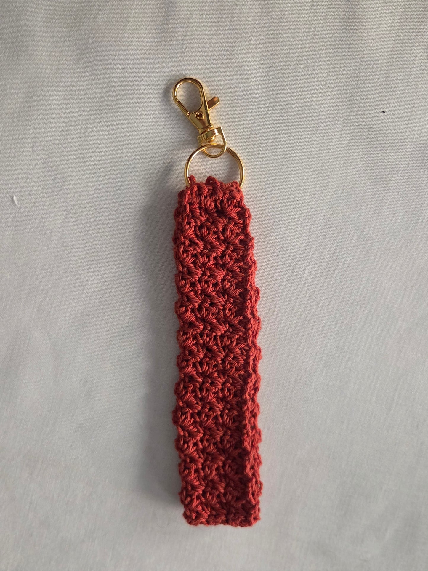 Handmade red crochet keychain with gold clasp on white fabric background