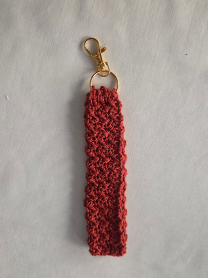 Handmade red crochet keychain with gold clasp on white fabric background