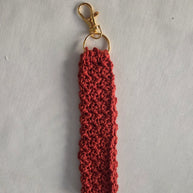 Handmade red crochet keychain with gold clasp on white fabric background