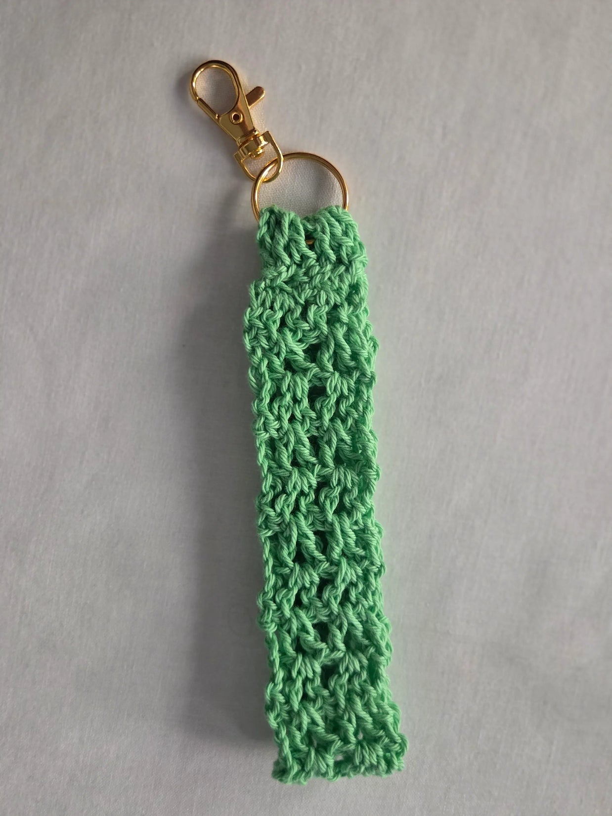 Mint green crochet keychain with gold clasp on light gray background.