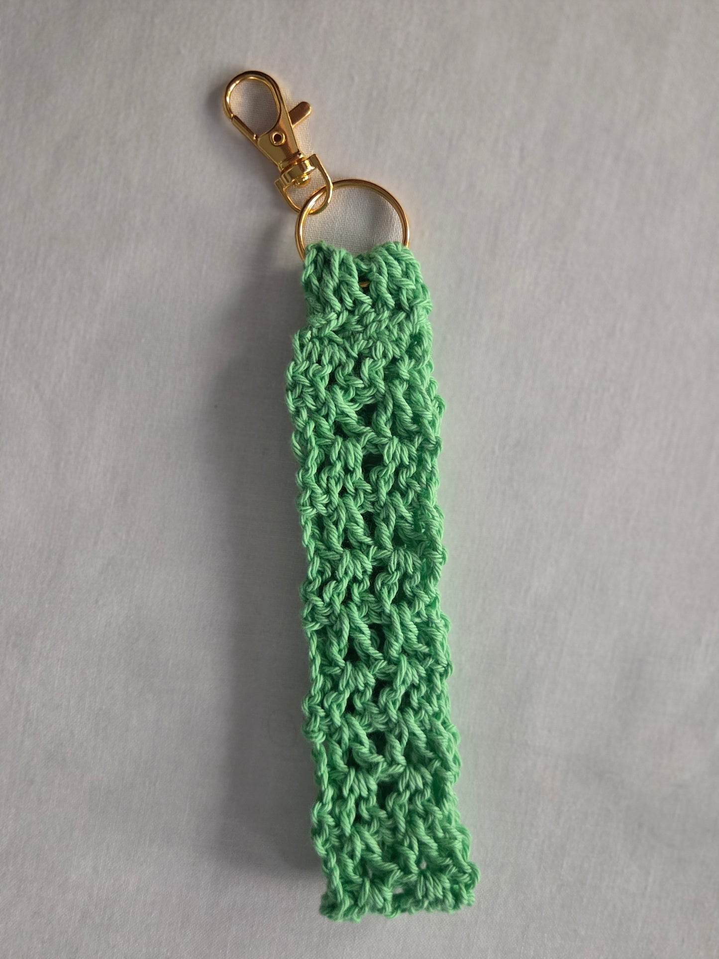 Mint green crochet keychain with gold clasp on light gray background.