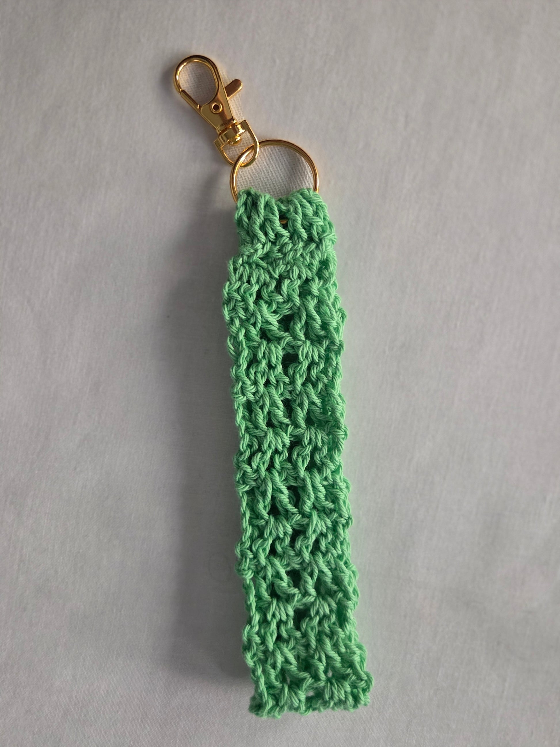 Mint green crochet keychain with gold clasp on light gray background.
