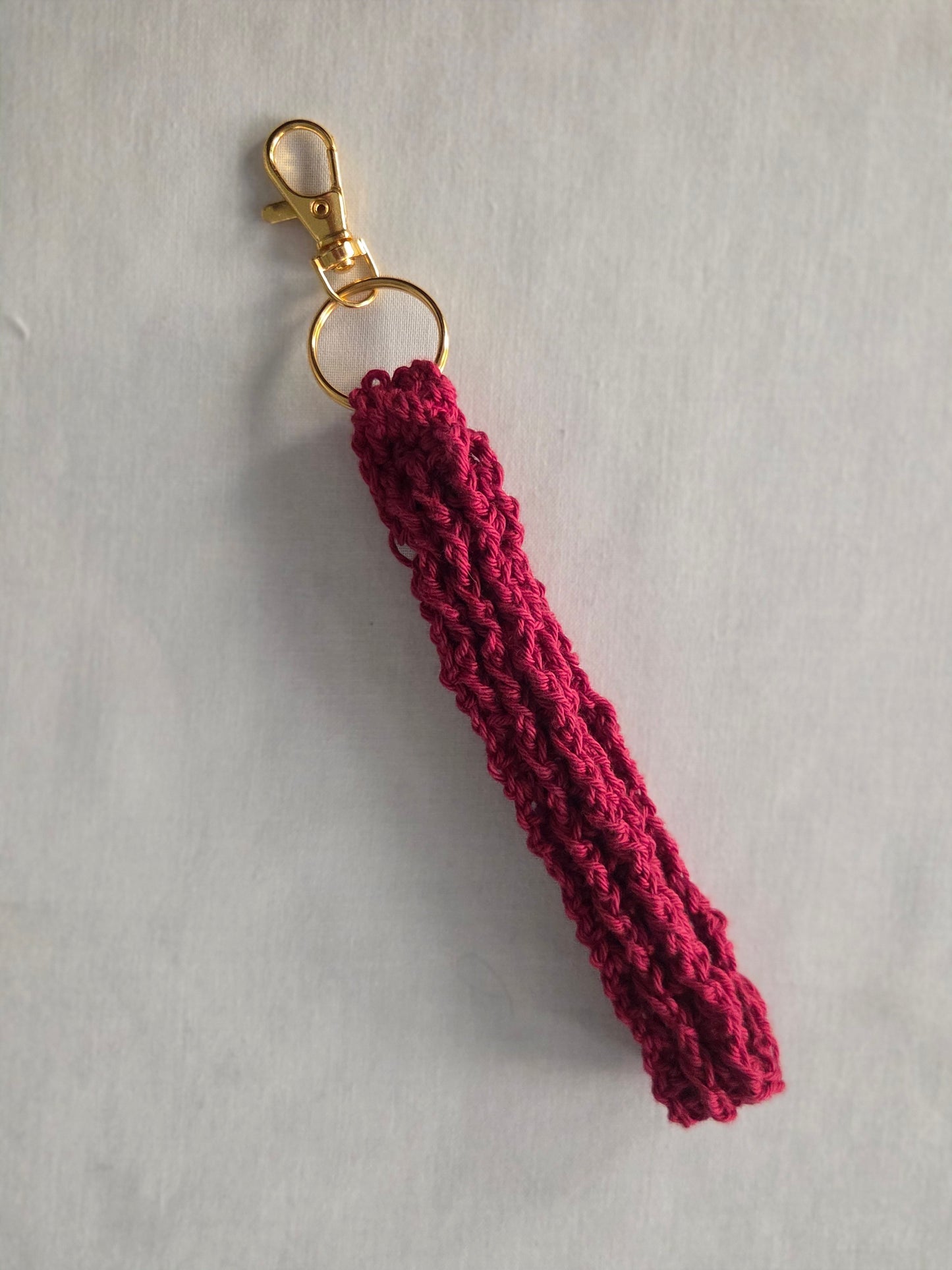 Handmade maroon crochet keychain with gold clasp on light background