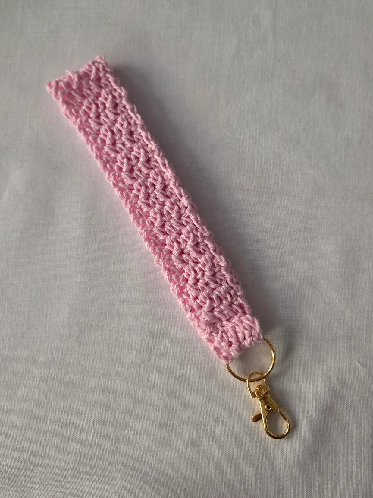 Handmade pink crochet keychain wristlet with gold clasp on white background