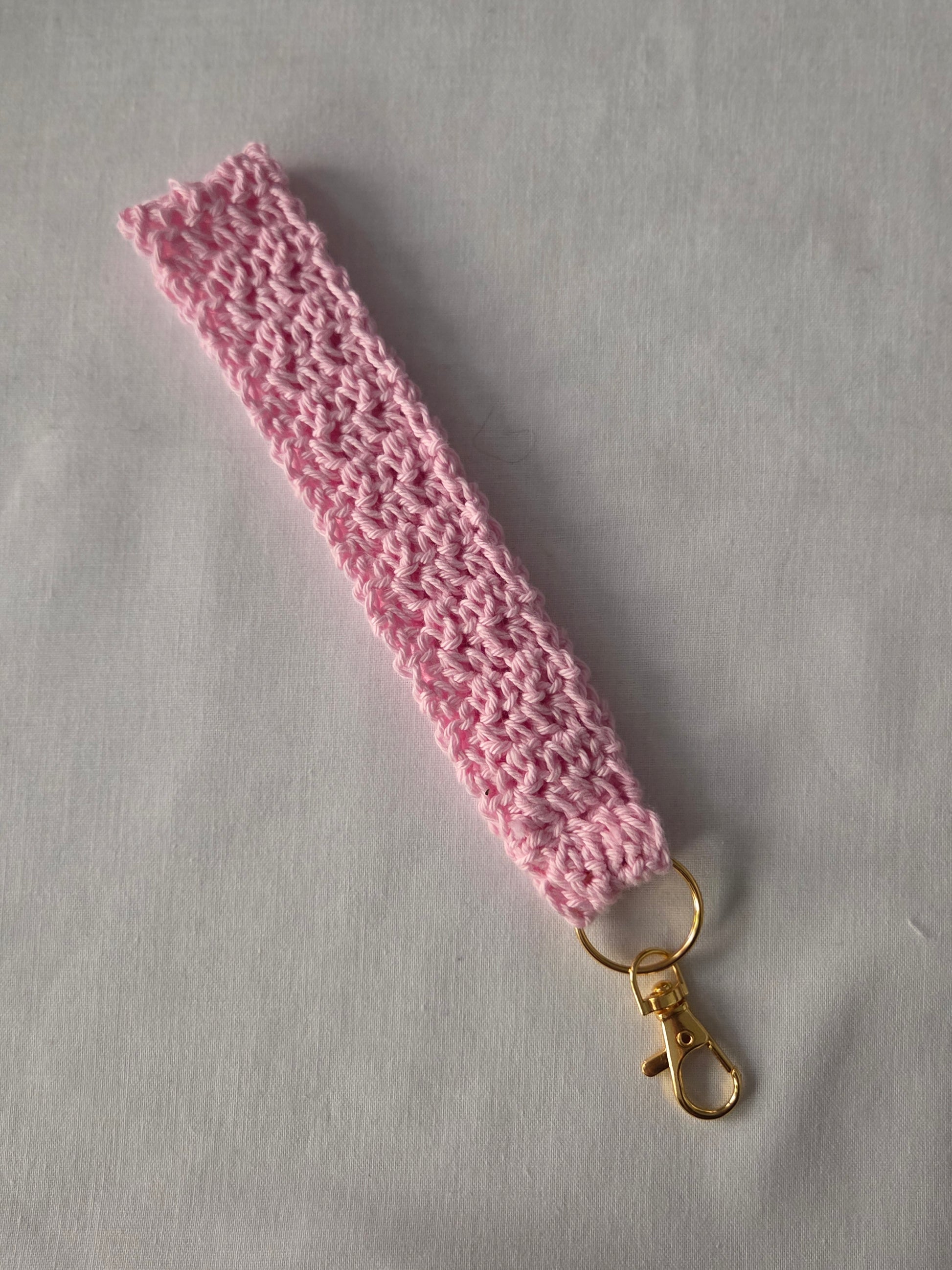 Handmade pink crochet keychain wristlet with gold clasp on white background
