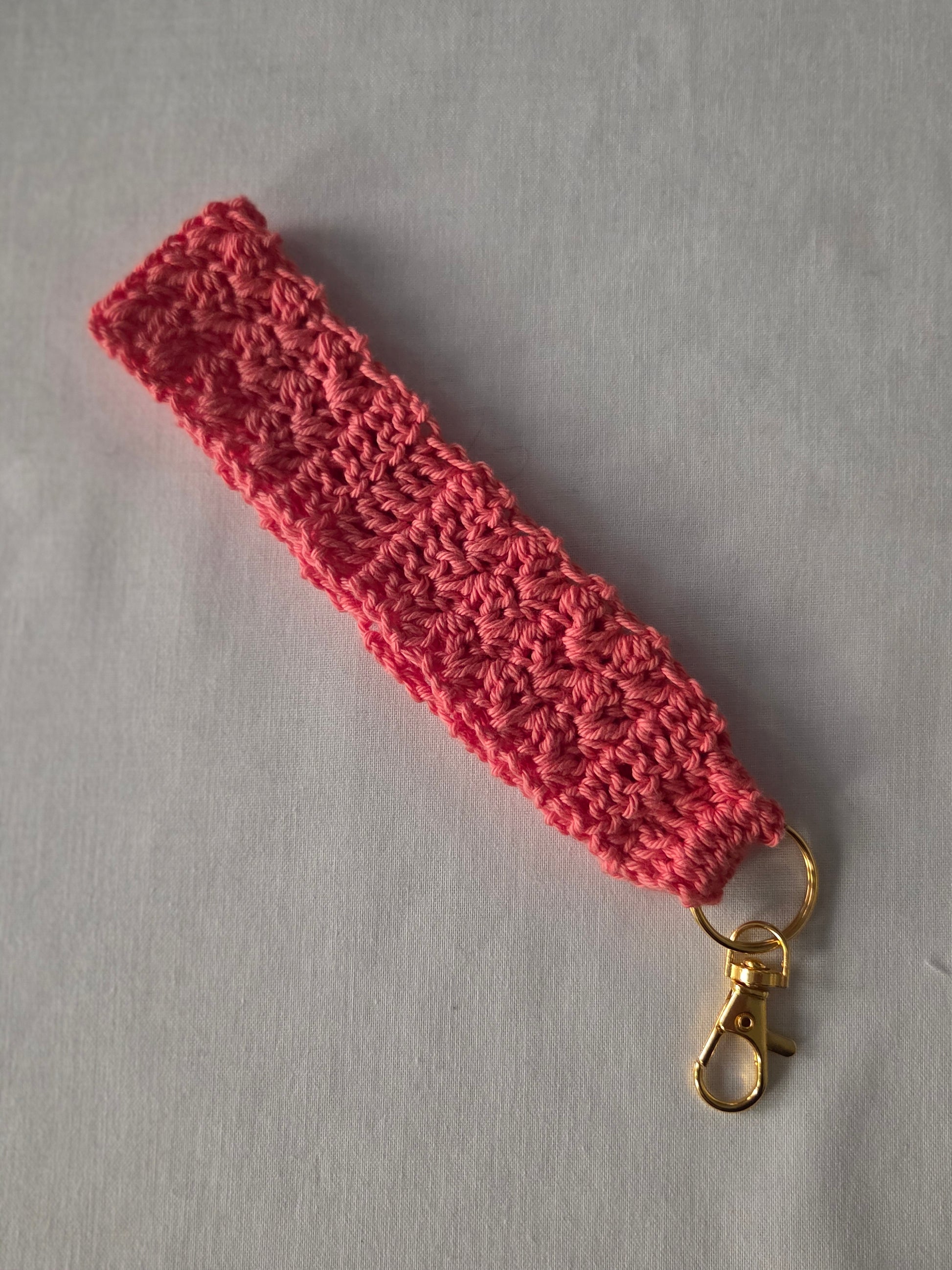 Pink crochet wristlet keychain with gold clasp on light background