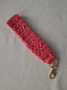 Pink crochet wristlet keychain with gold clasp on light background