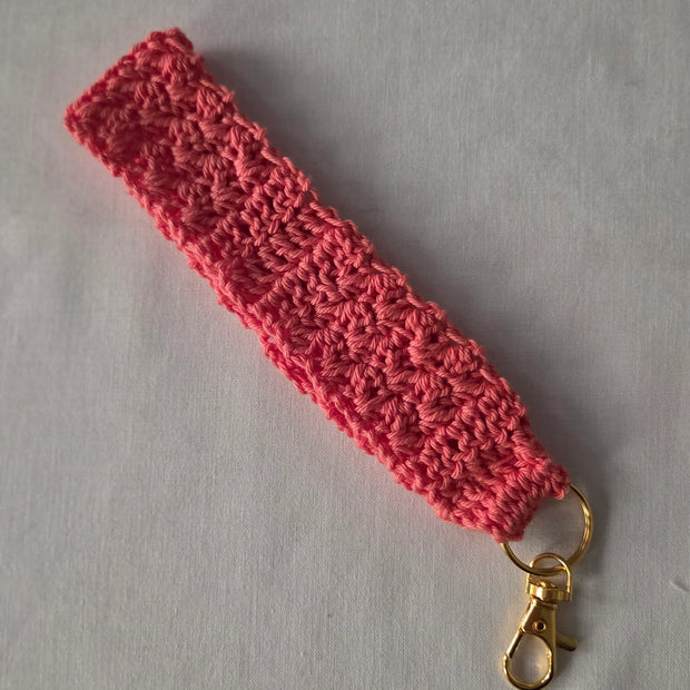 Pink crochet wristlet keychain with gold clasp on light background