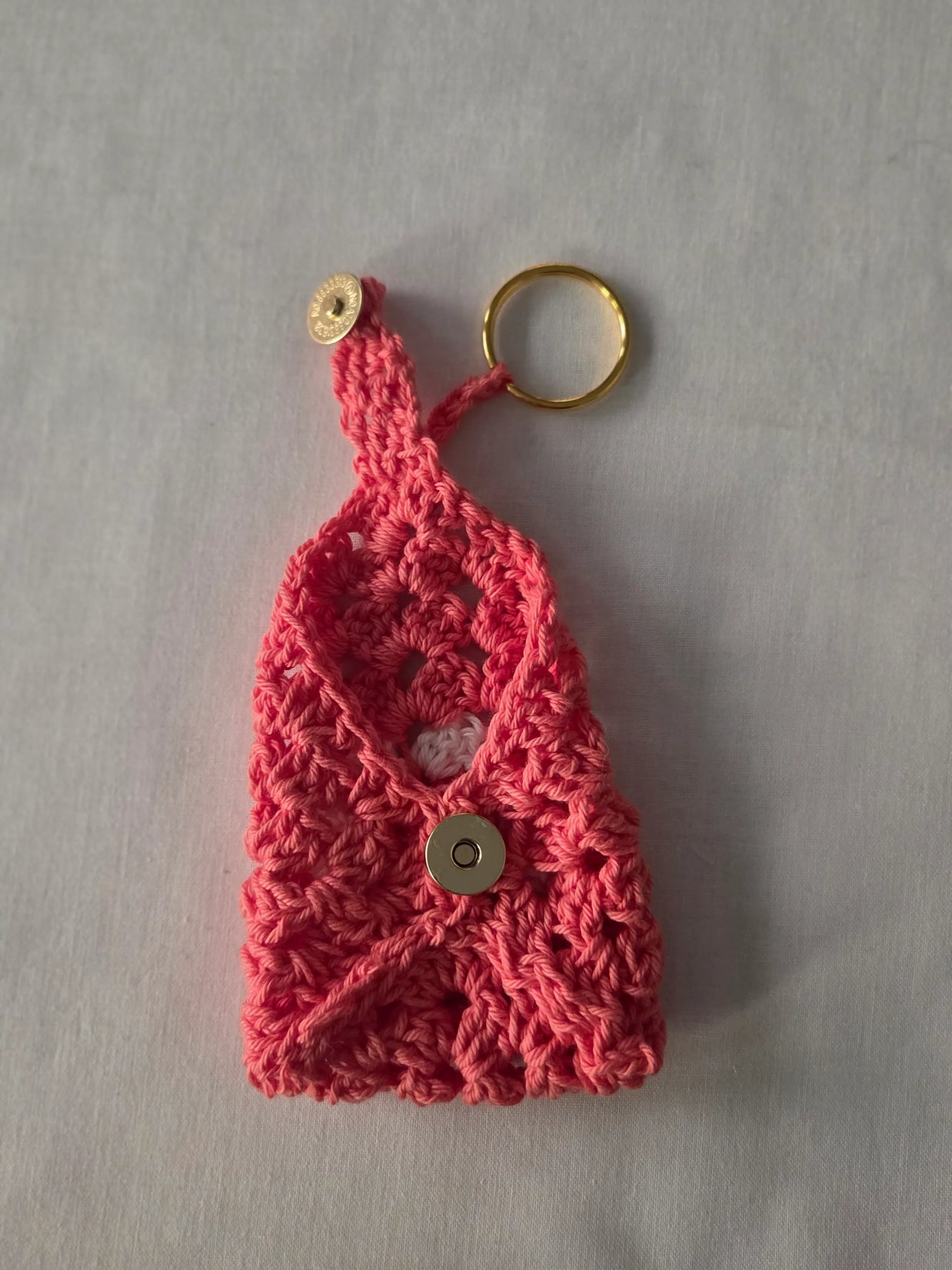 Handmade pink crochet keychain pouch with gold snap button and keyring on light fabric