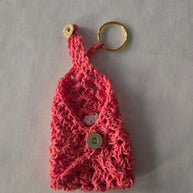 Handmade pink crochet keychain pouch with gold snap button and keyring on light fabric