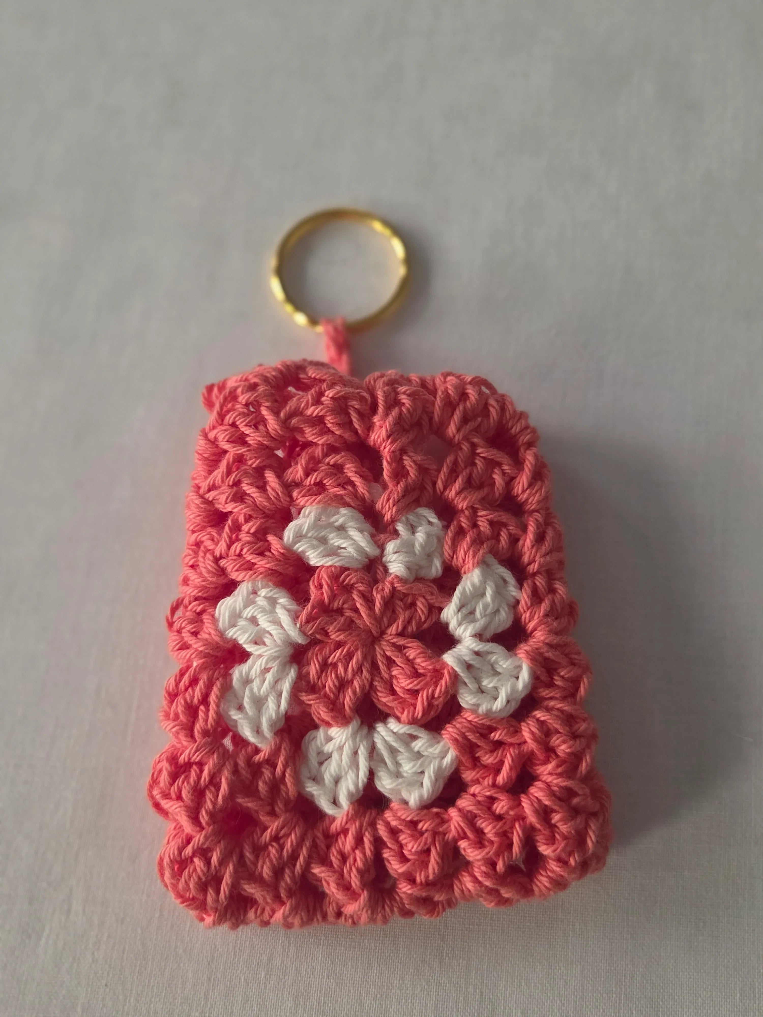 Handmade crochet keychain with pink and white flower pattern on a white background