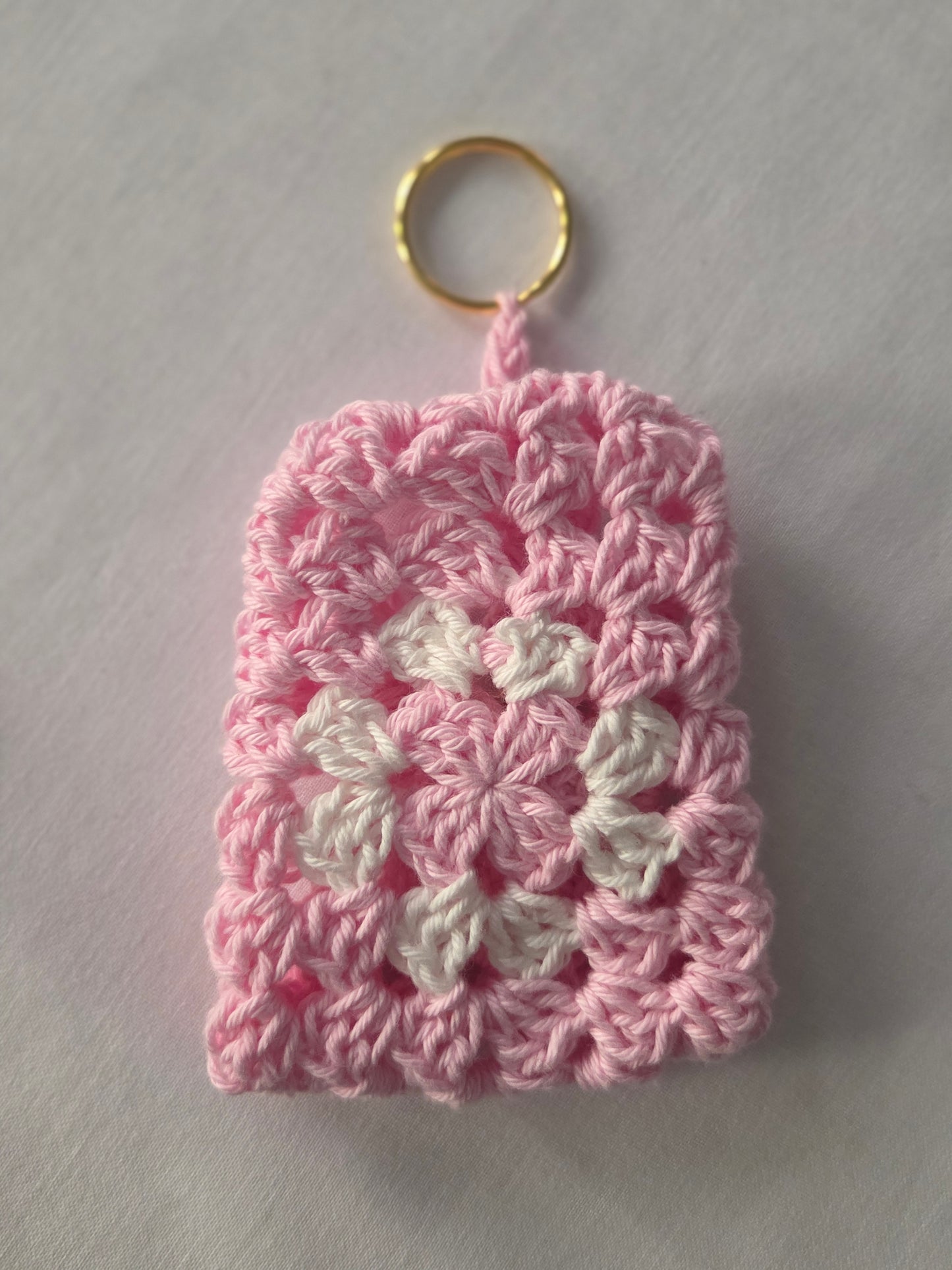 Pink and white crochet keychain pouch with gold ring on white background