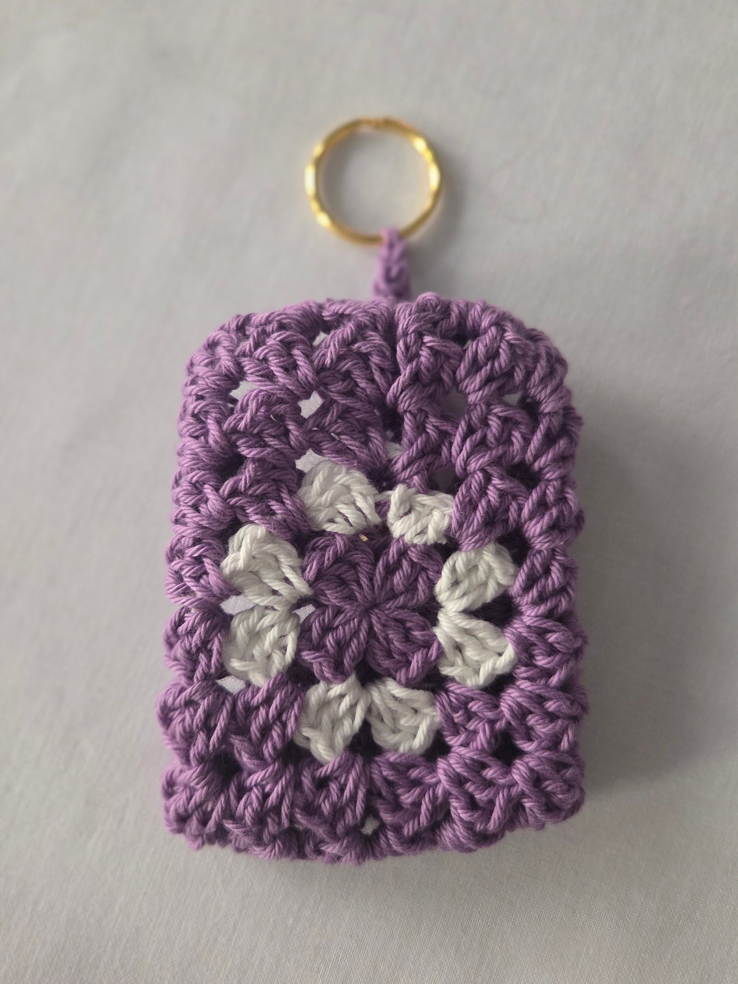 Purple and white crochet granny square keychain with gold ring on white background