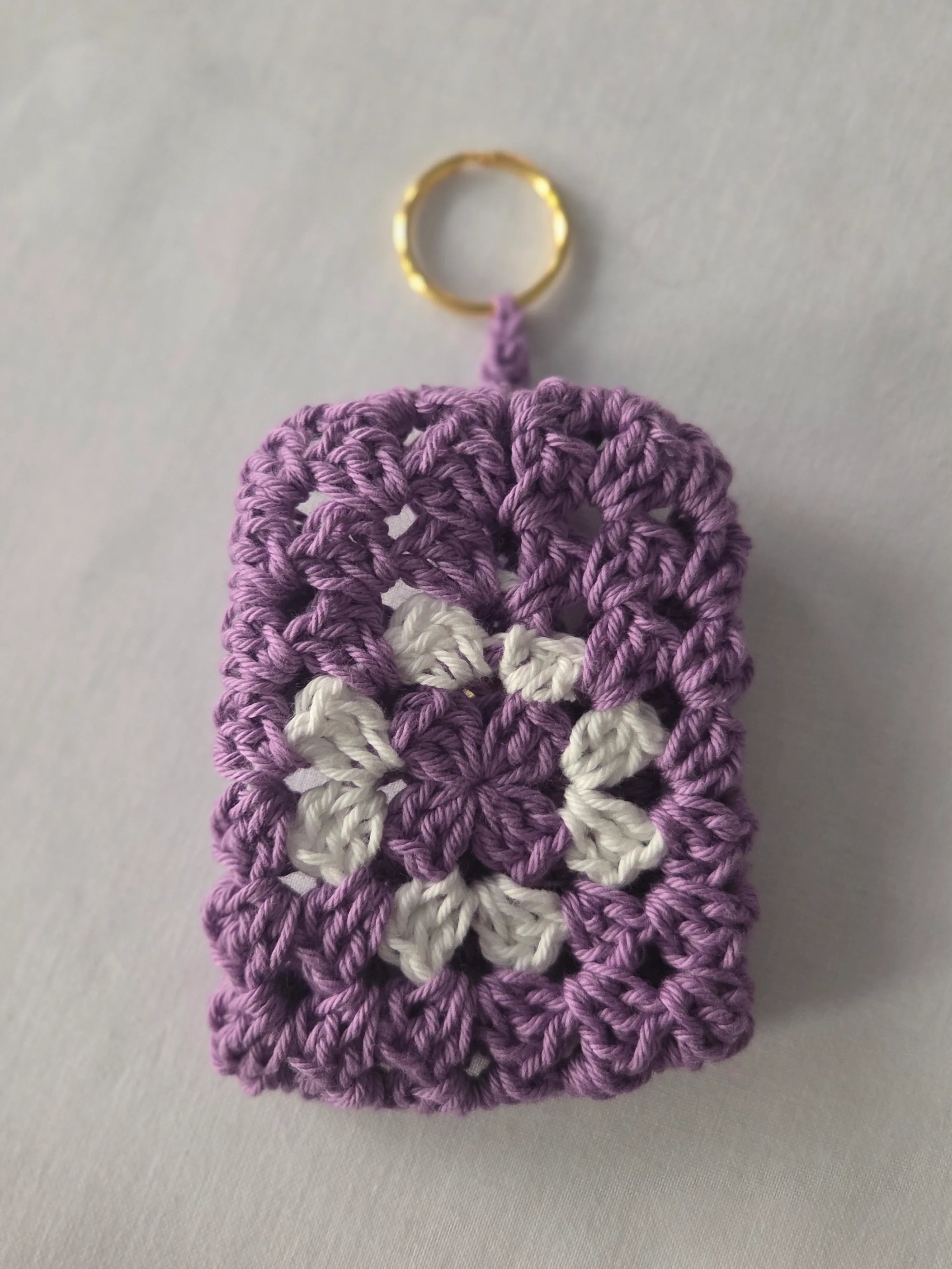 Purple and white crochet granny square keychain with gold ring on white background
