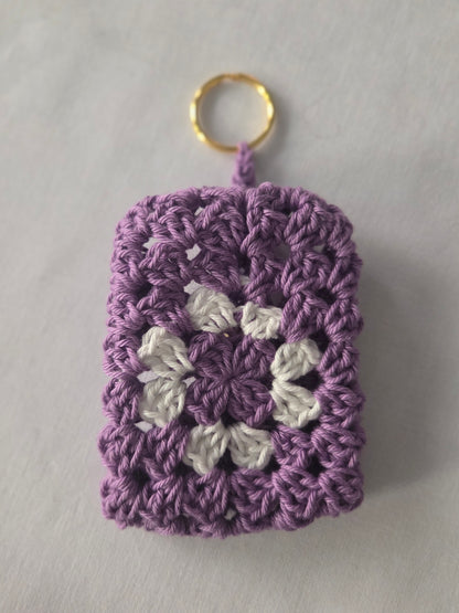 Purple and white crochet granny square keychain with gold ring on white background