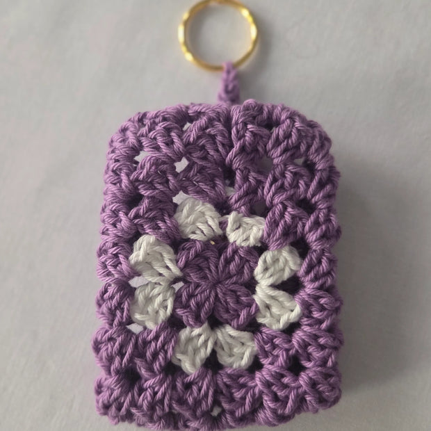 Purple and white crochet granny square keychain with gold ring on white background