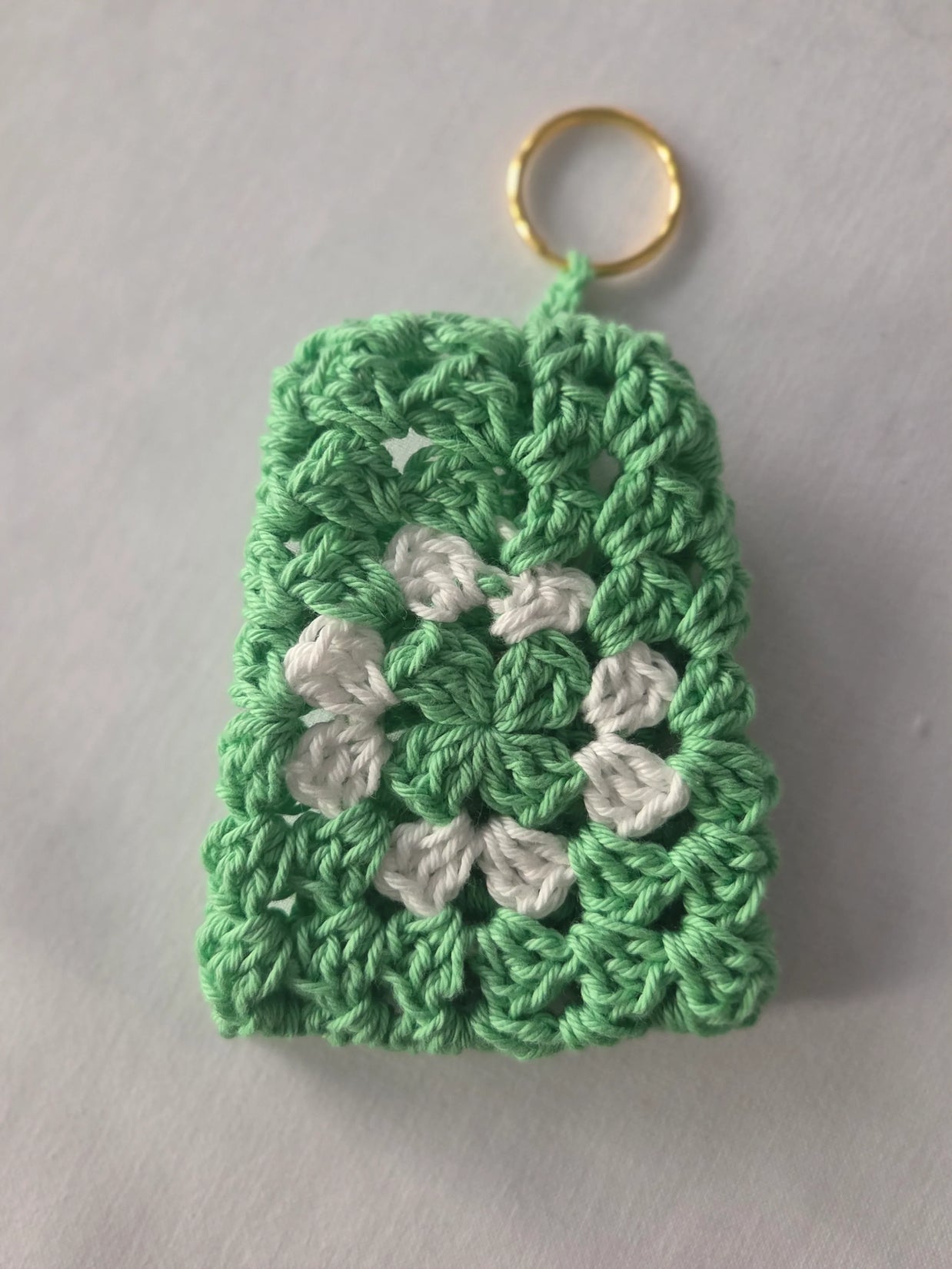 Green and white crochet keychain with granny square pattern on white background