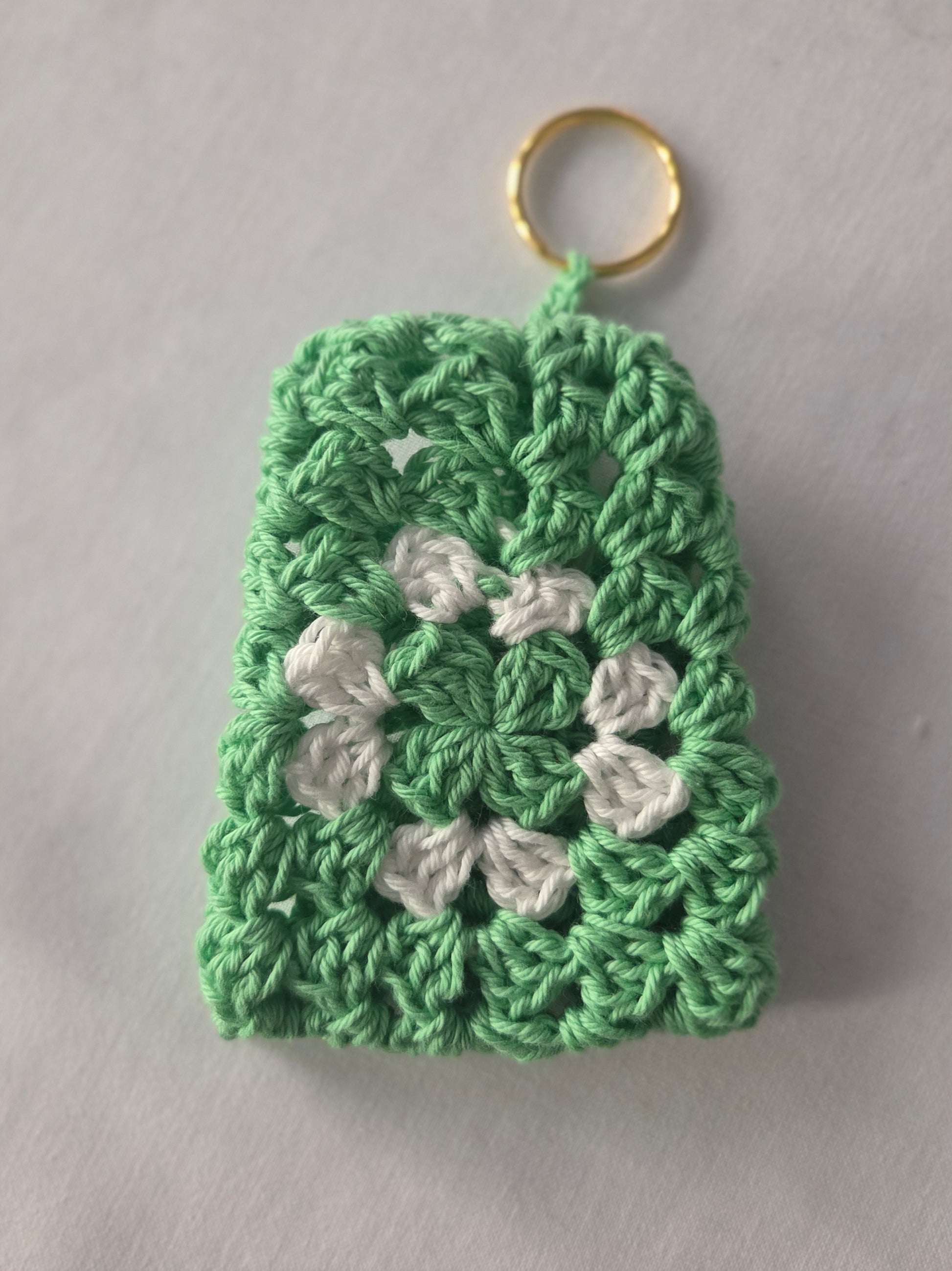 Green and white crochet keychain with granny square pattern on white background