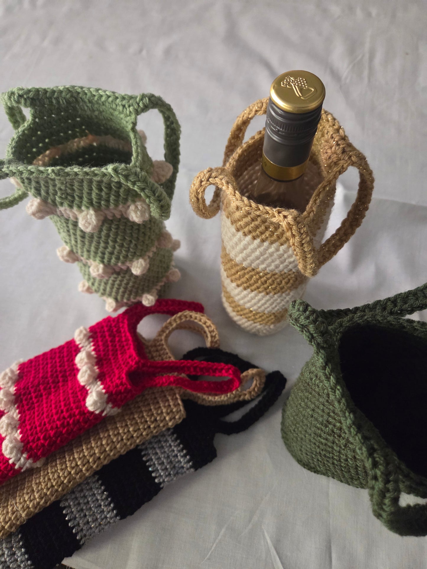 Handmade crochet wine bottle holders in various colors on a white tablecloth