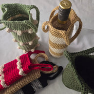Handmade crochet wine bottle holders in various colors on a white tablecloth