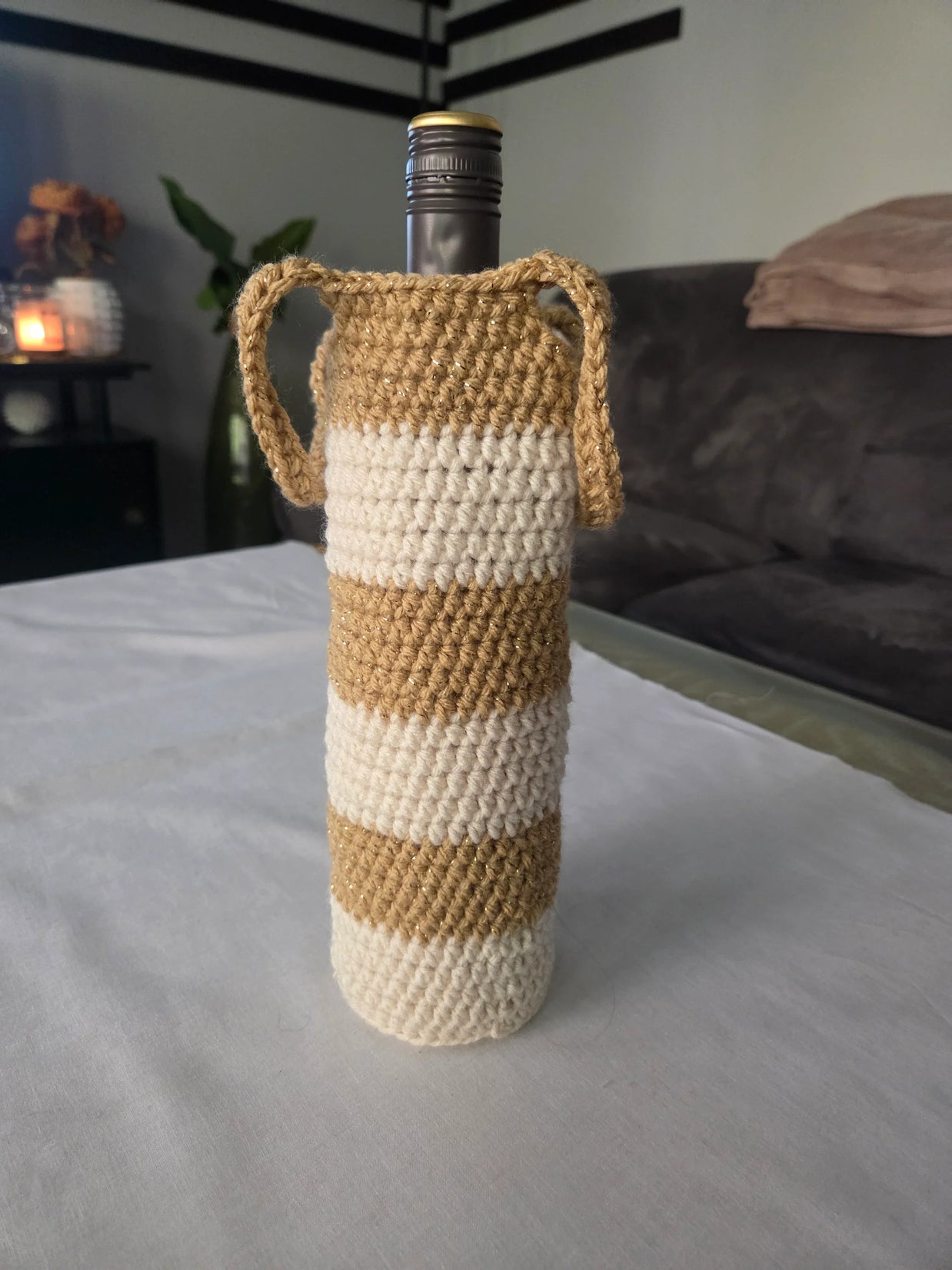Wine bottle in beige and white striped crochet cover with handles on table indoors