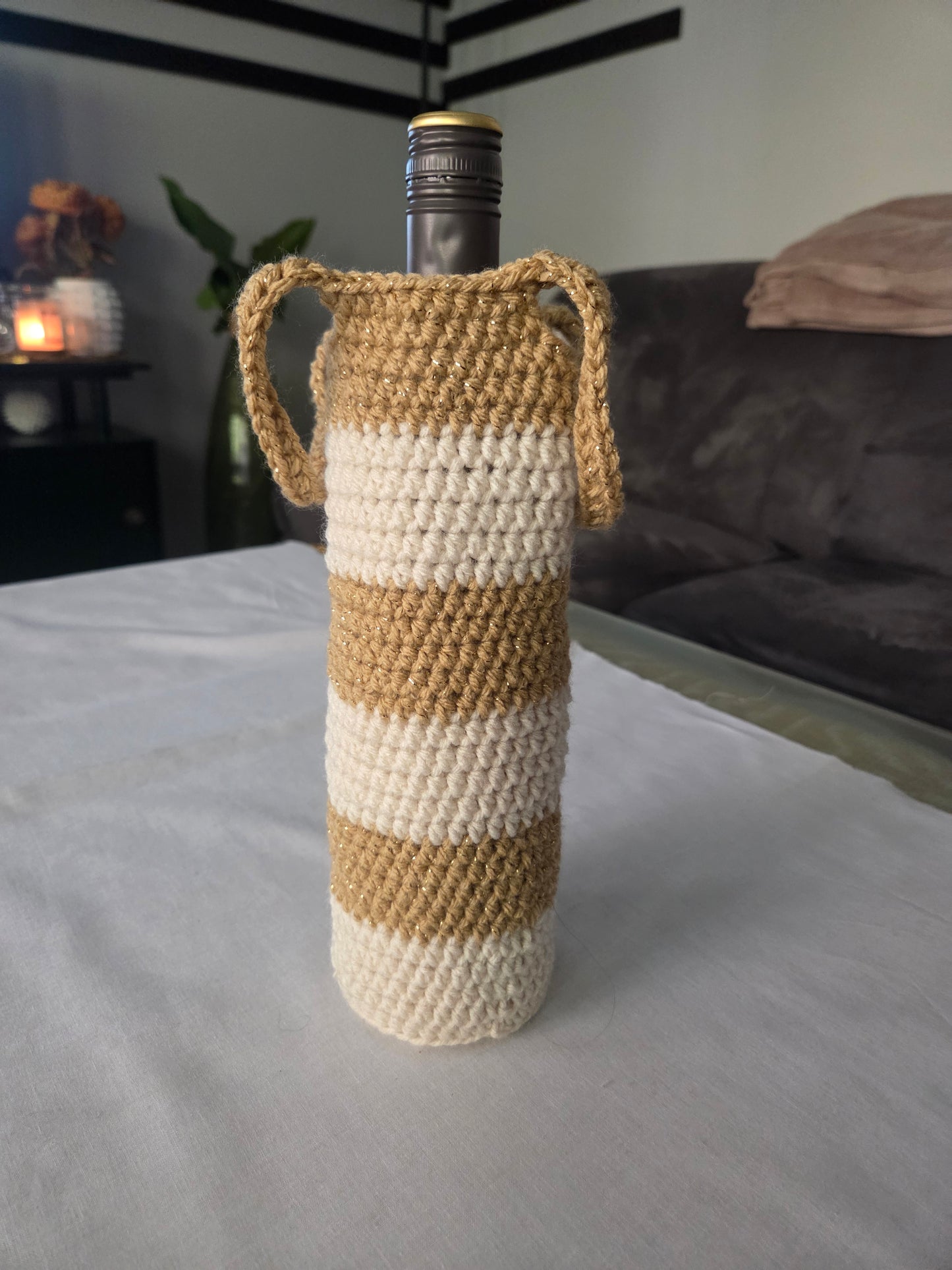 Wine bottle in beige and white striped crochet cover with handles on table indoors
