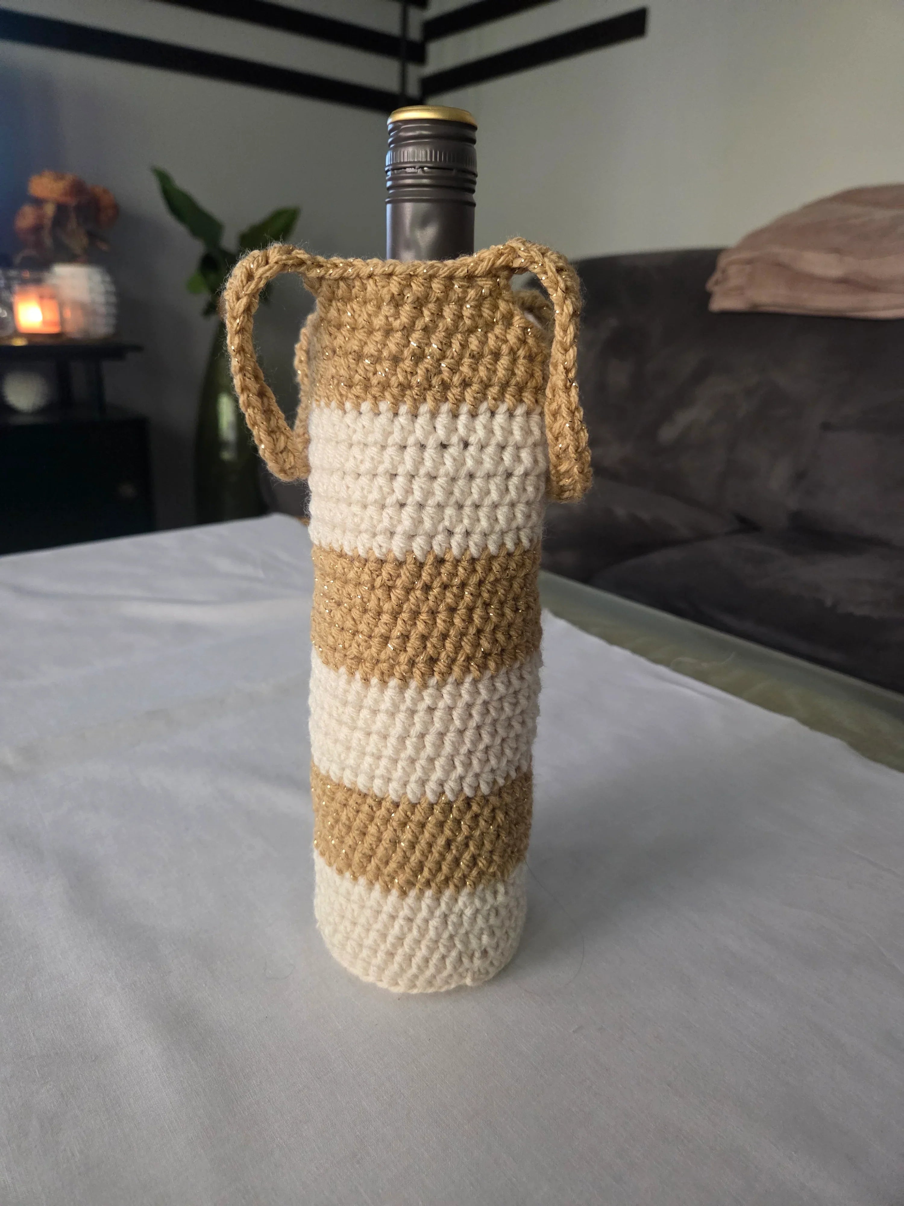 Wine bottle in beige and white striped crochet cover with handles on table indoors