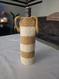 Wine bottle in beige and white striped crochet cover with handles on table indoors