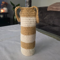 Wine bottle in beige and white striped crochet cover with handles on table indoors