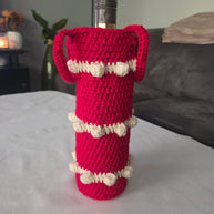Red crochet wine bottle cover with white bobble accents on table
