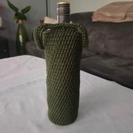 Green crochet wine bottle cover on table with grey couch in background
