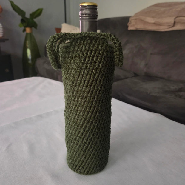 Green crochet wine bottle cover on table with grey couch in background