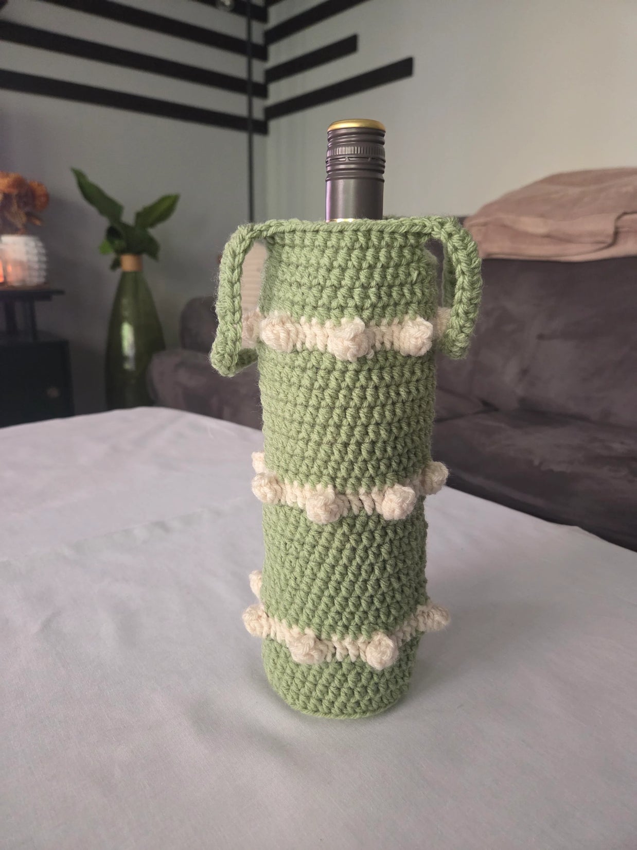 Green crochet wine bottle holder with white accents on table in cozy living room