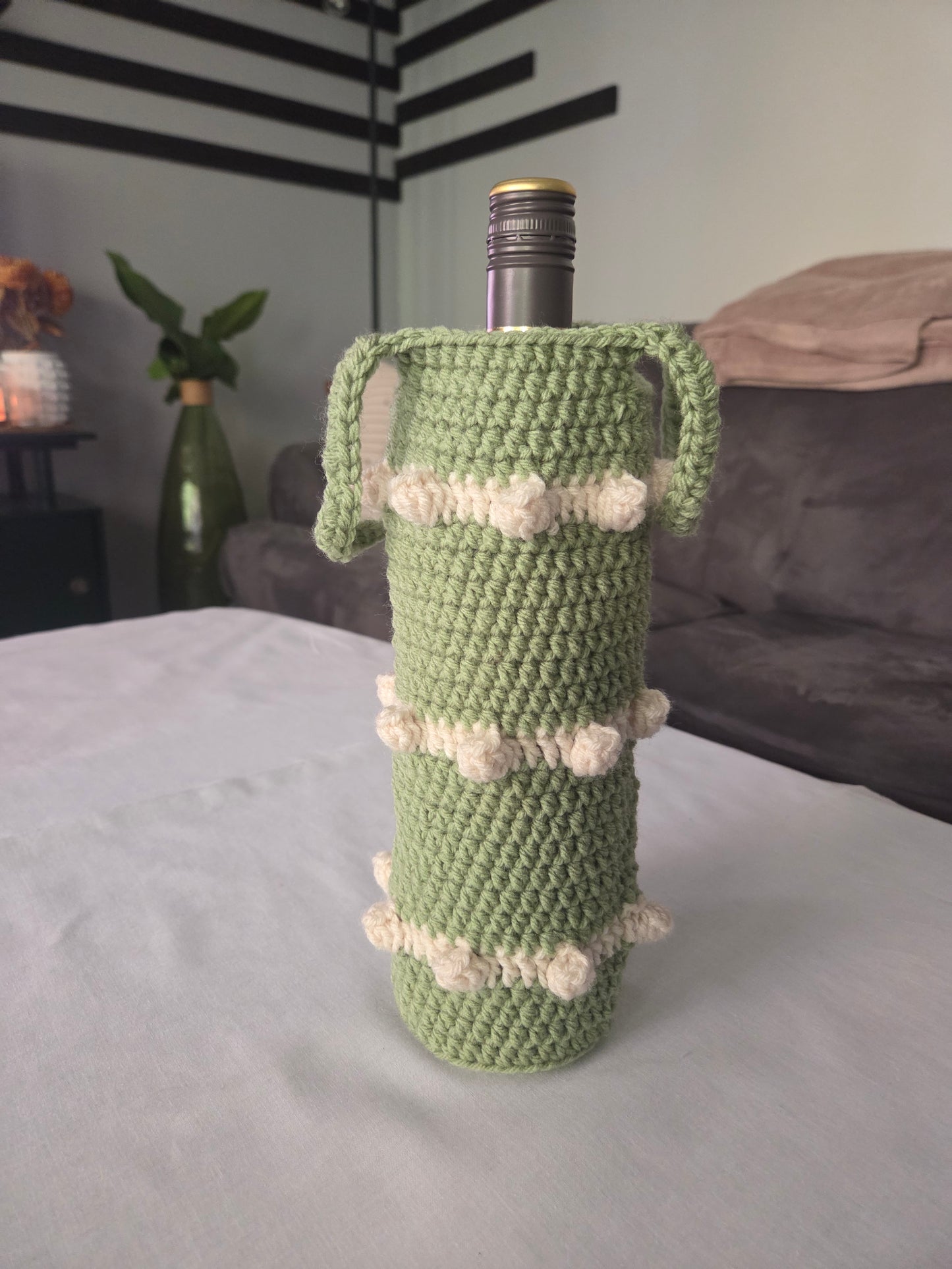 Green crochet wine bottle holder with white accents on table in cozy living room