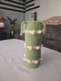 Green crochet wine bottle holder with white accents on table in cozy living room