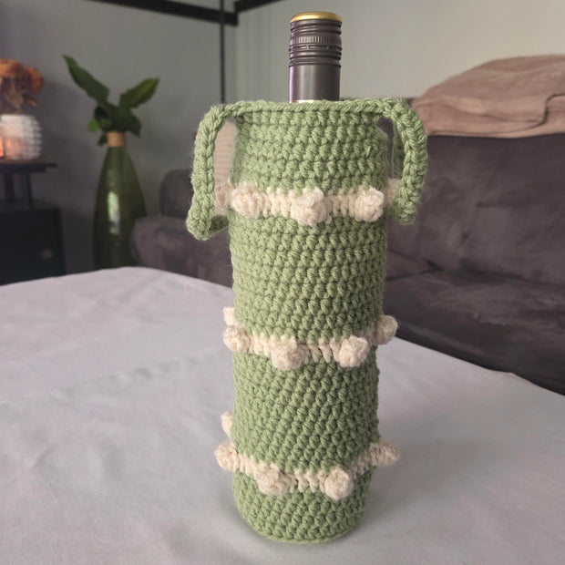 Green crochet wine bottle holder with white accents on table in cozy living room