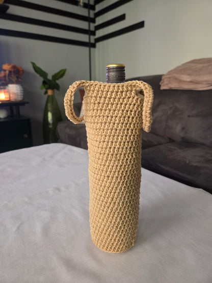 Beige crochet wine bottle cover with handles on a white table in a modern living room.