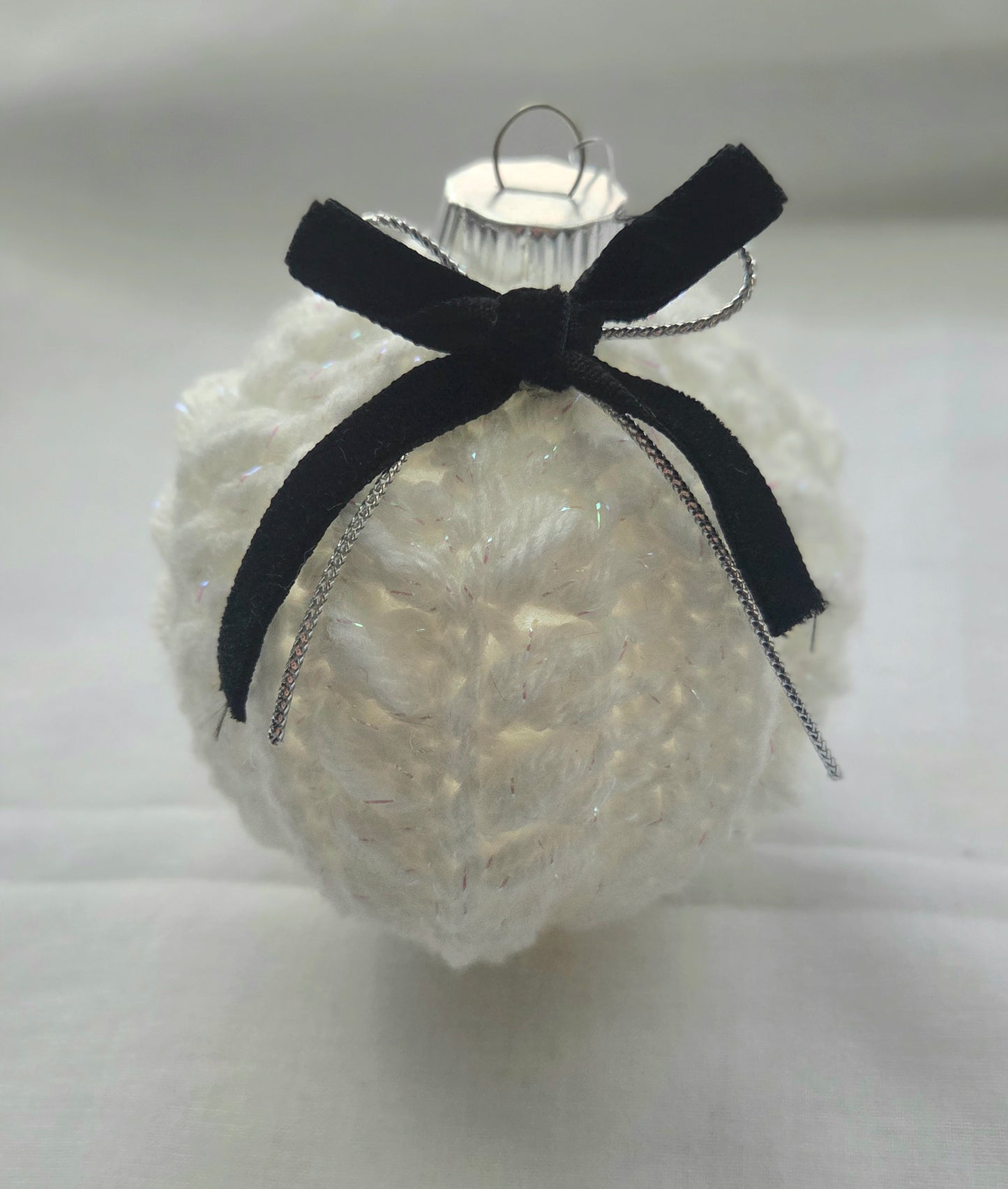 White knitted Christmas ornament with black velvet bow on plain background