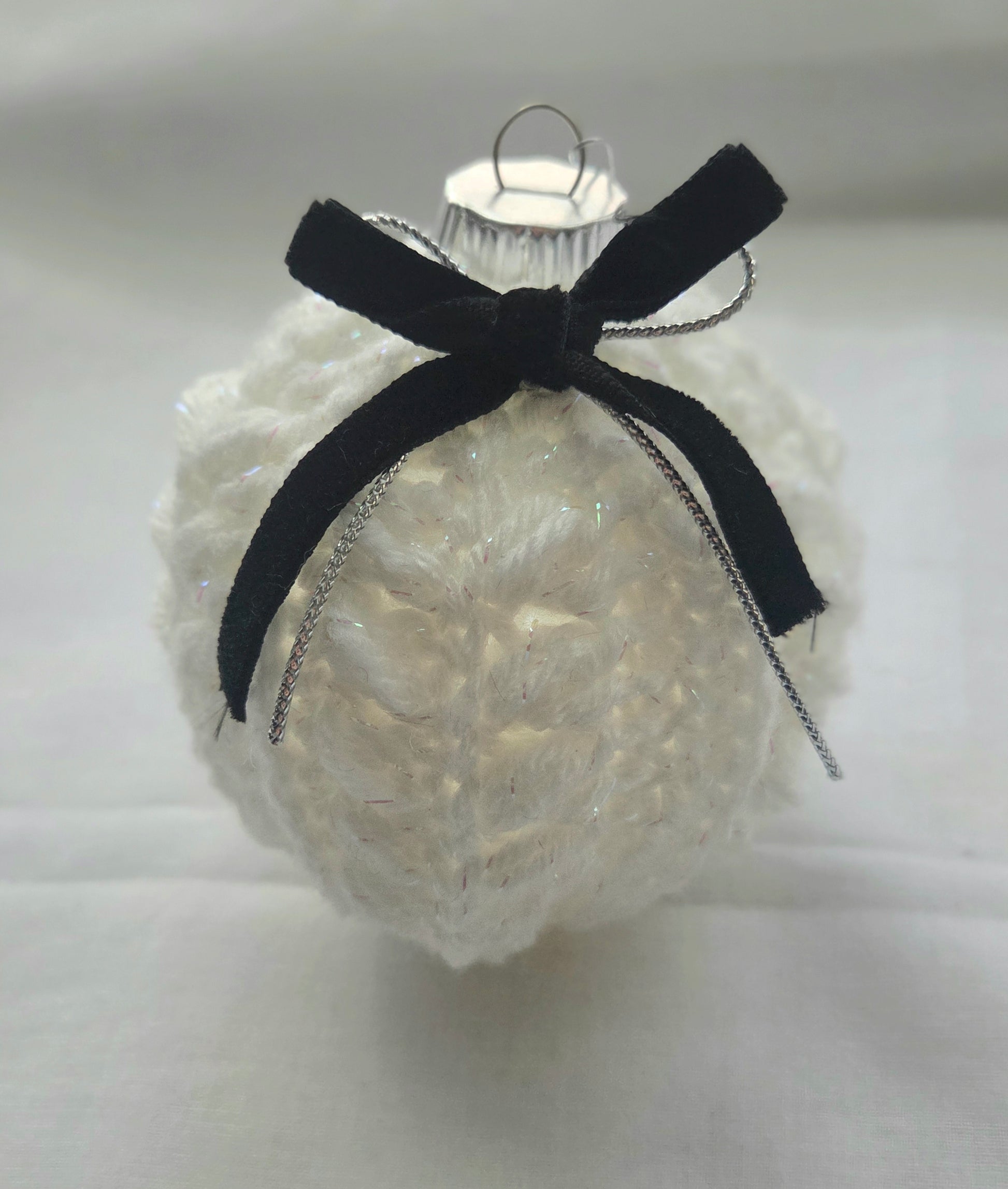 White knitted Christmas ornament with black velvet bow on plain background