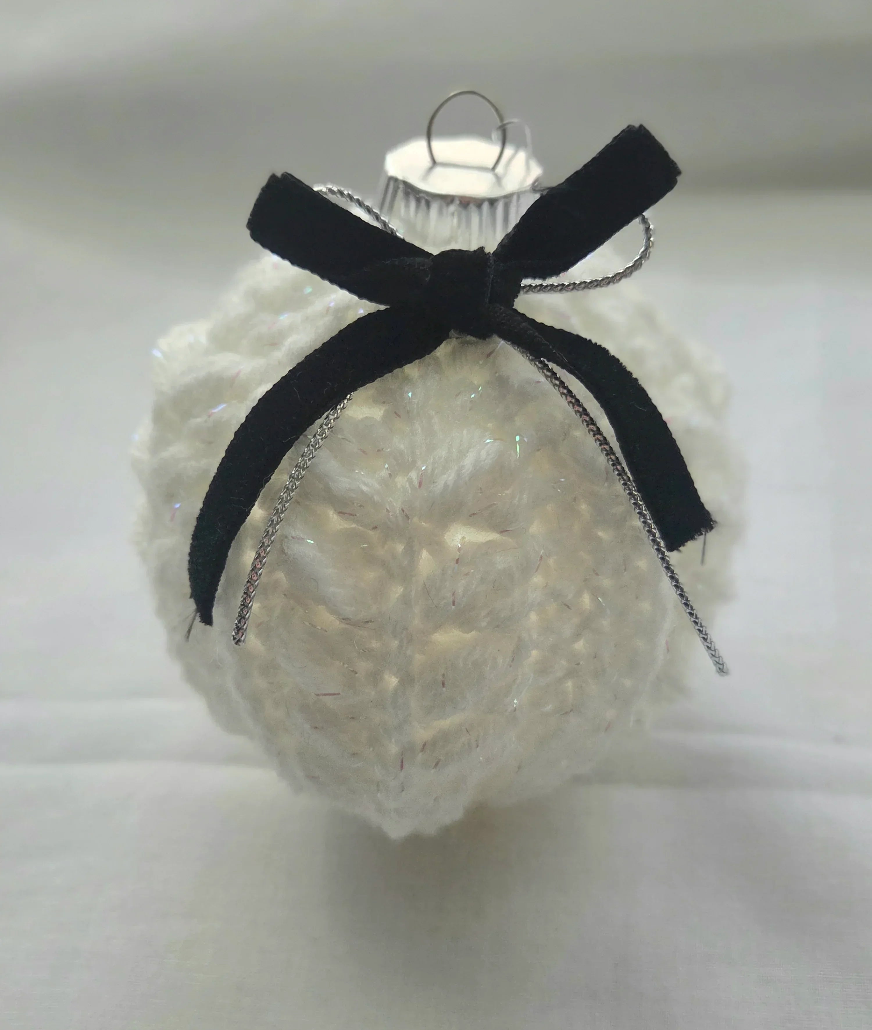 White knitted Christmas ornament with black velvet bow on plain background