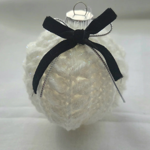 White knitted Christmas ornament with black velvet bow on plain background