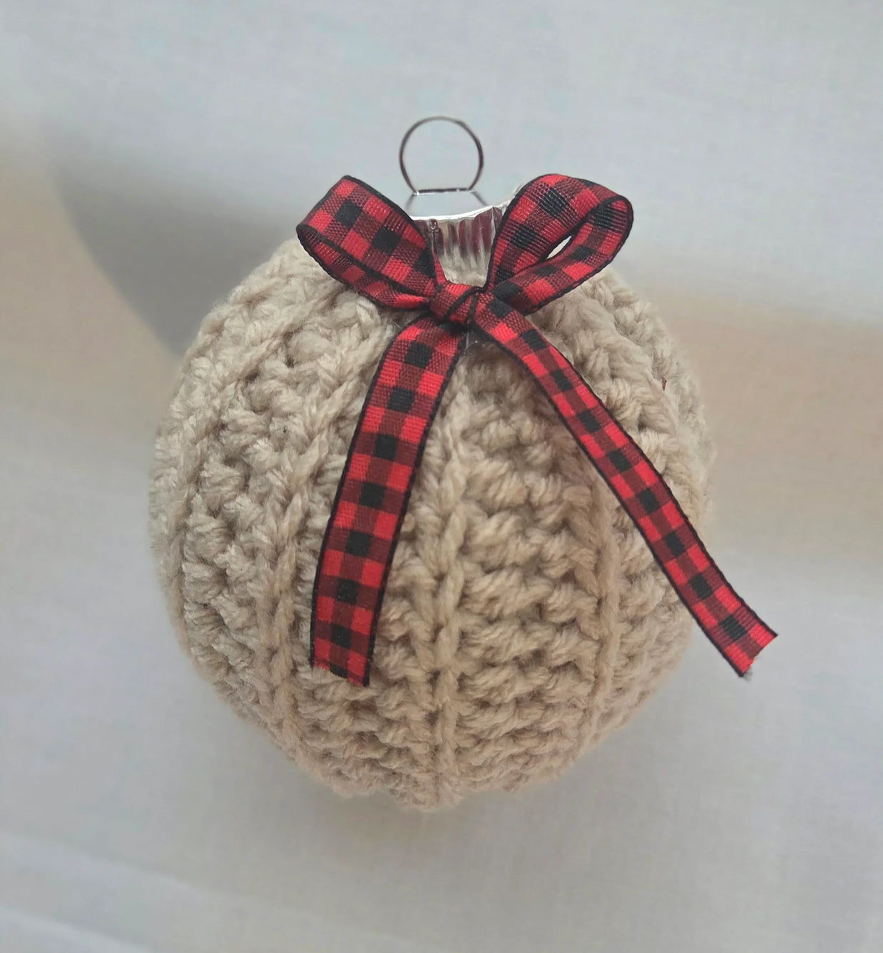 Crocheted Christmas ornament with red plaid bow on white background
