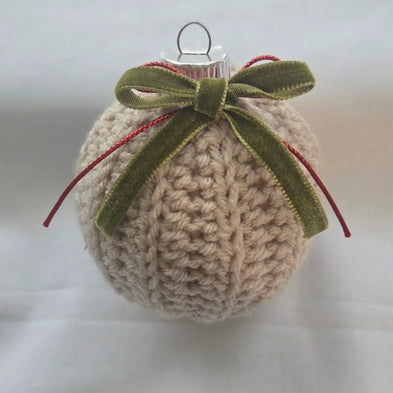 Knitted beige Christmas ornament with green velvet bow and red ribbon on white background