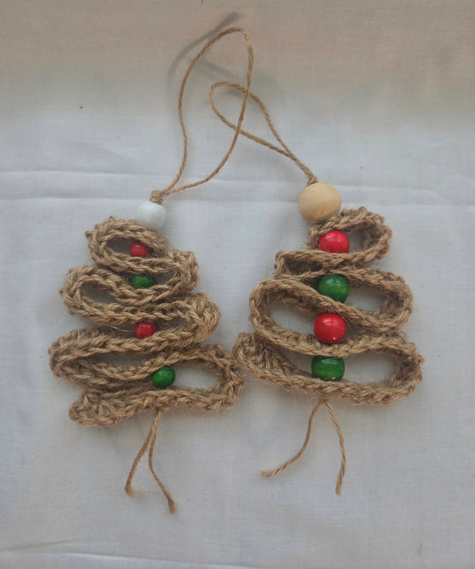 Handmade jute Christmas tree ornaments with red and green beads on white background
