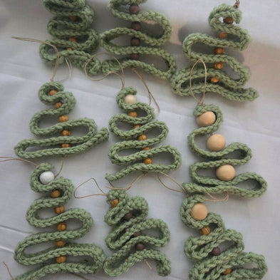 Handmade crochet Christmas tree ornaments with wooden beads on a white fabric background.