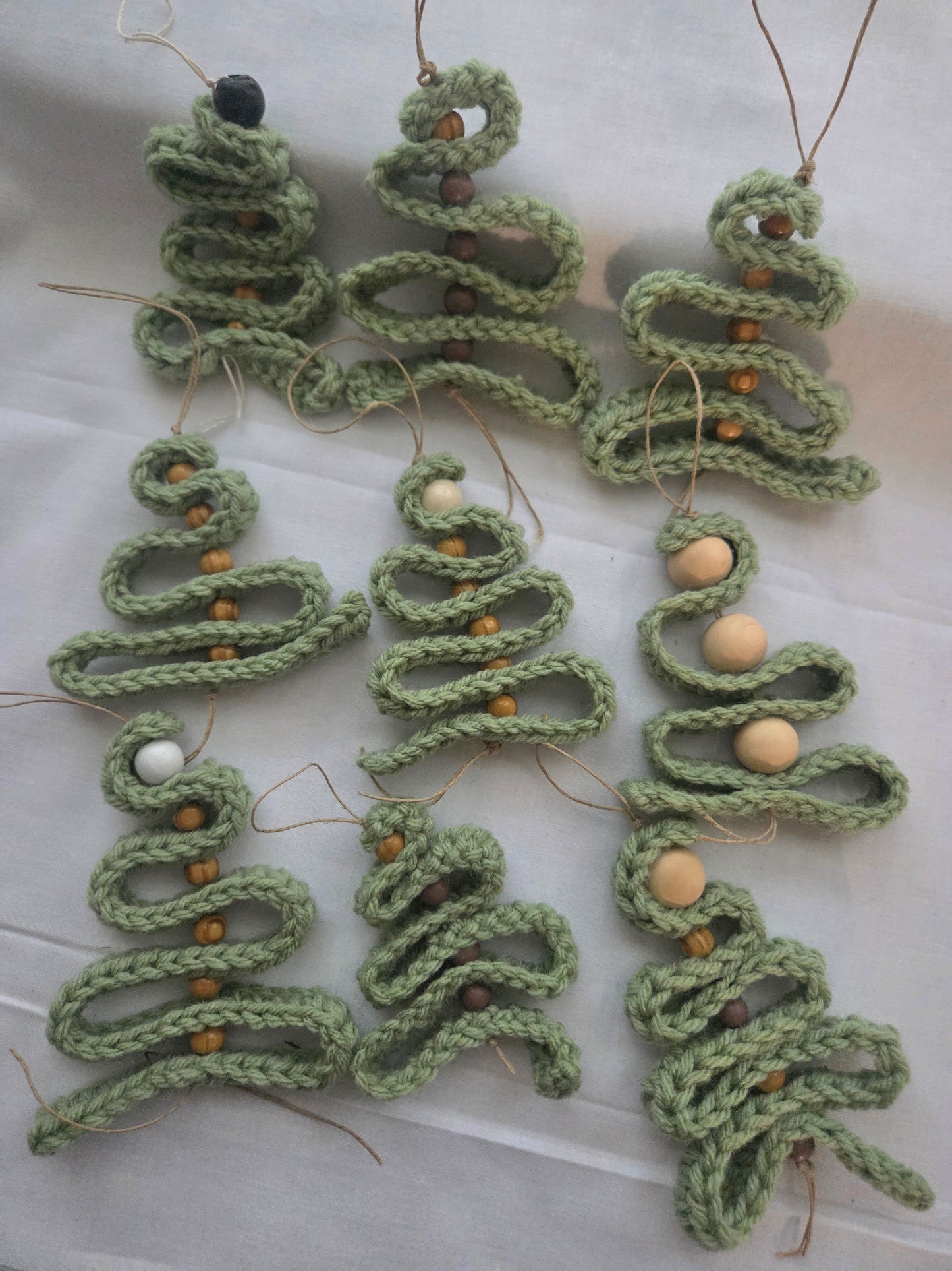 Handmade crochet Christmas tree ornaments with wooden beads on a white fabric background.
