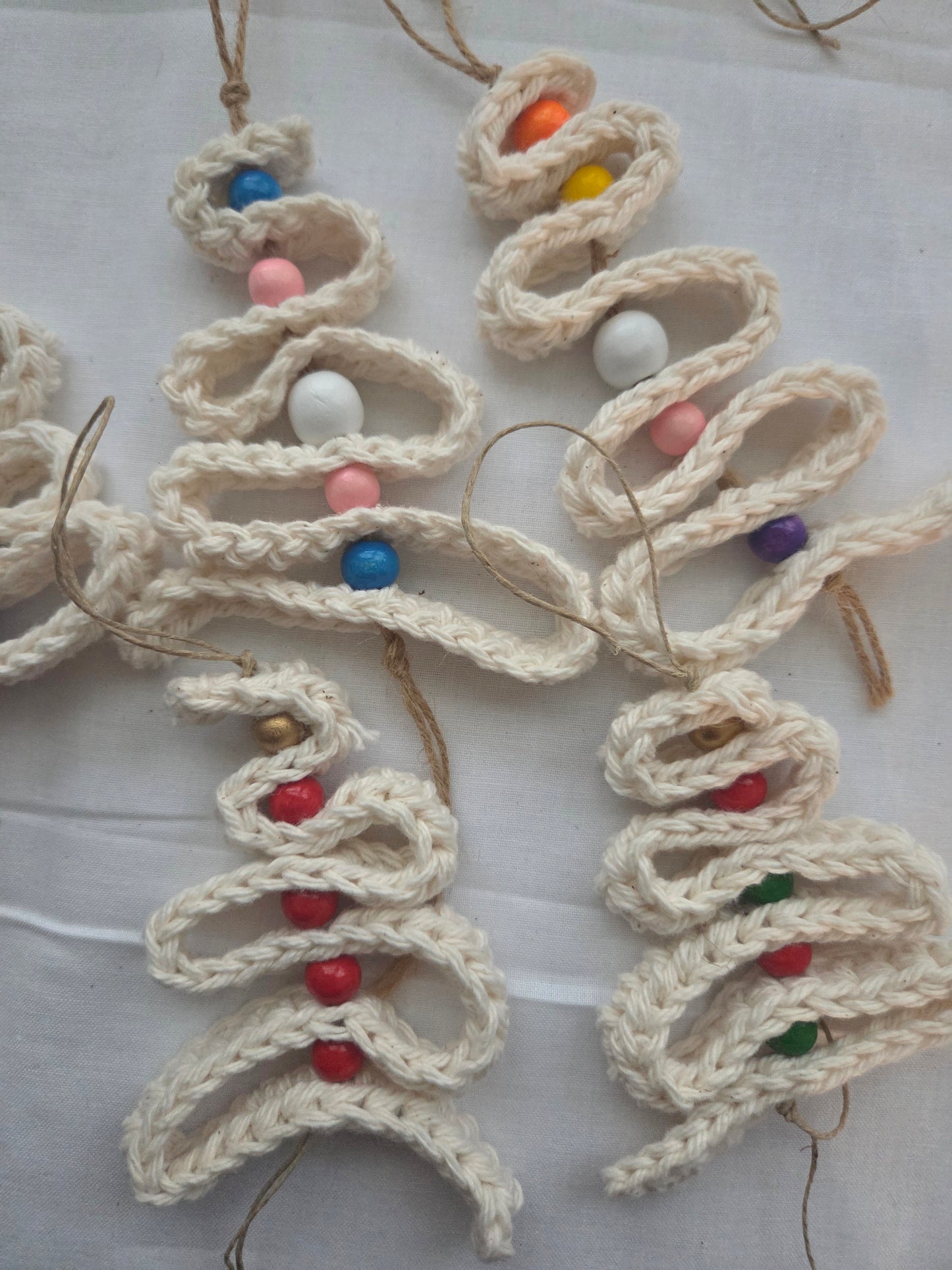Handmade crochet Christmas tree ornaments with colorful beads on white fabric